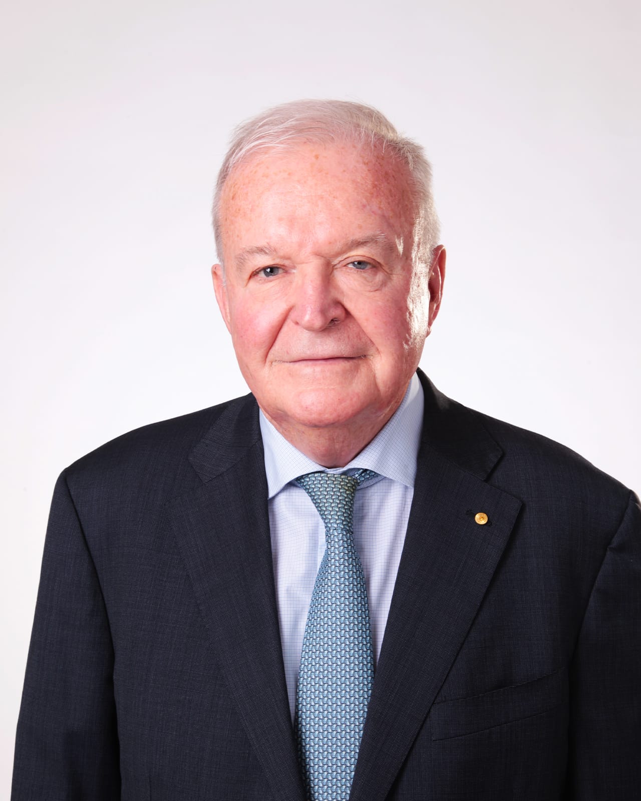 Portrait of older man with gray hair, wearing a suit, light blue shirt, and patterned blue tie.